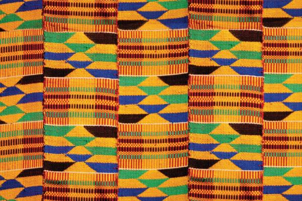 A colorful, tightly-woven textile with repeating vertical bands of geometric patterns. The colors include various shades of yellow, green, blue, brown, and red.