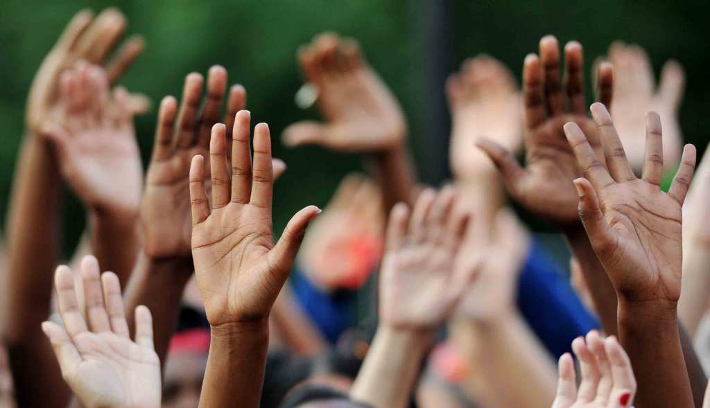 A close up shot of many hands with different skin colors raised in the air together.