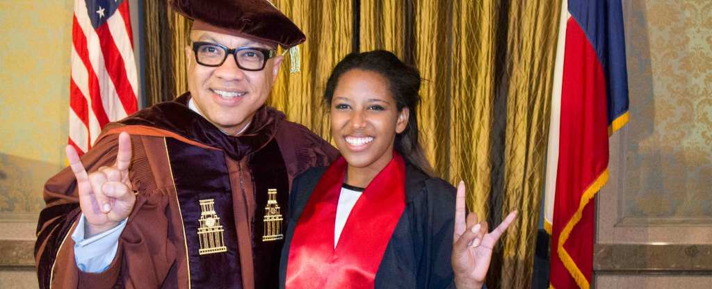 Darren Walker poses with a University of Texas graduate in graduation robes. They are both smiling and using the Hook 'em Horns hand sign.