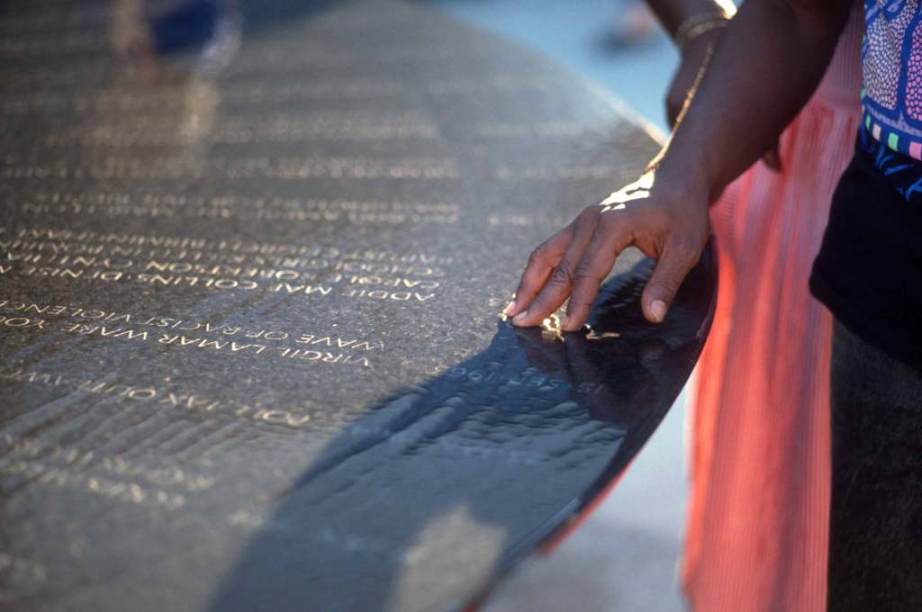 A closeup shot of a Black person's hand resting gently on the water table at the Civil Rights Memorial in Montgomery, Alabama.