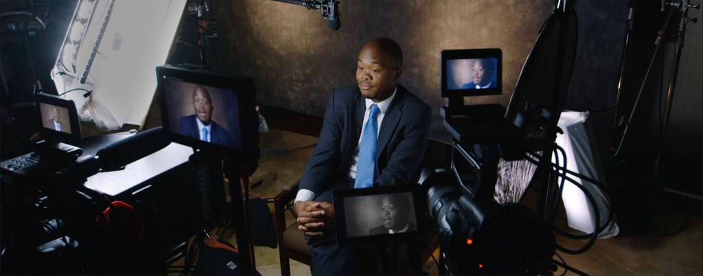 Fred Swaniker sits in front of a backdrop with multiple cameras capturing his interview from different angles.