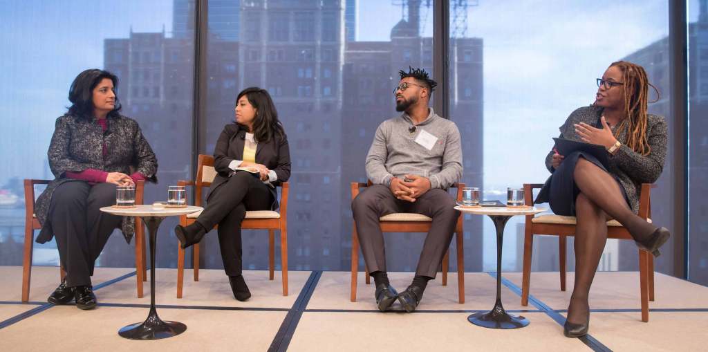 Heather McGhee leads a discussion onstage with Cristina Jimenez, managing director of United We Dream; Umi Selah, founder of Dream Defenders; and Farhana Khera, director of Muslim Advocates. They are all seated in front of a large window looking out at the city.