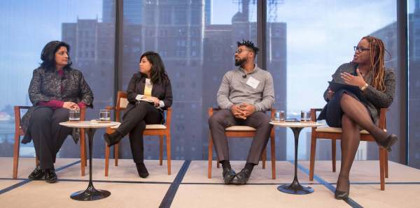 Heather McGhee leads a discussion onstage with Cristina Jimenez, managing director of United We Dream; Umi Selah, founder of Dream Defenders; and Farhana Khera, director of Muslim Advocates. They are all seated in front of a large window looking out at the city. 