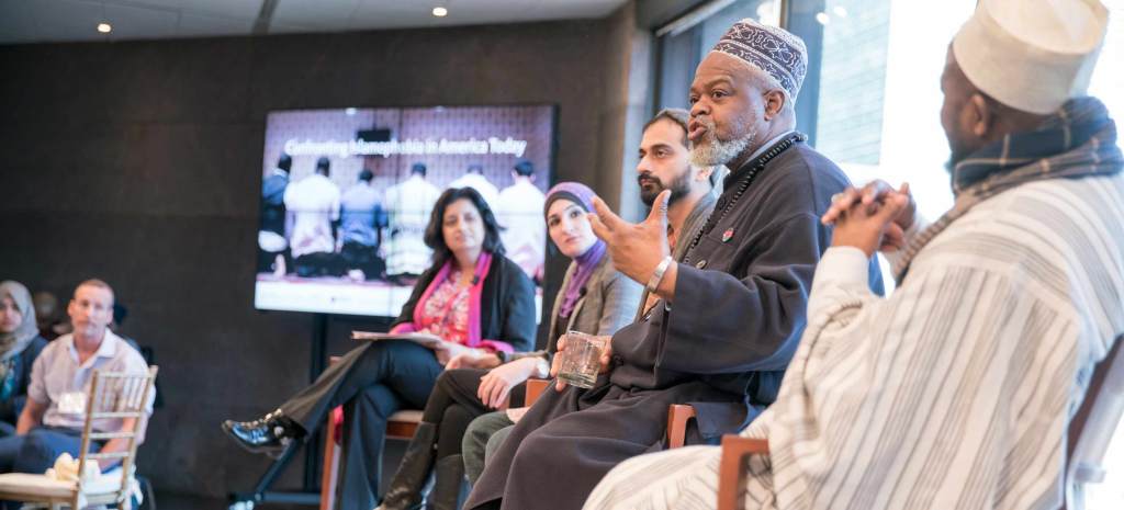 Five Muslim community members are on stage, speaking to an audience.