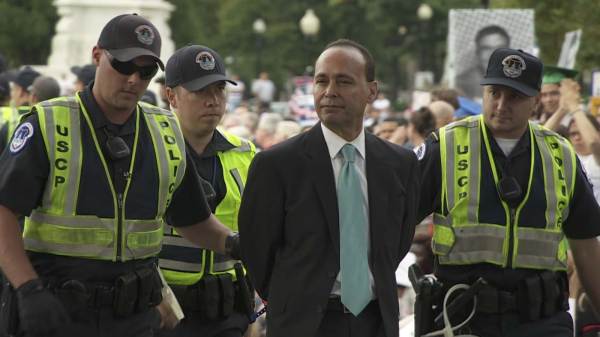 Police taking protester into custody. This image is unavailable under the 4.0 Creative Commons license.