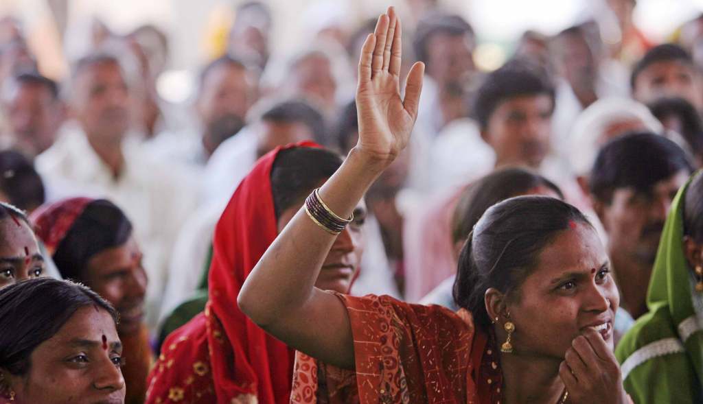 An Indian woman raises her hand to ask a question at a community meeting.