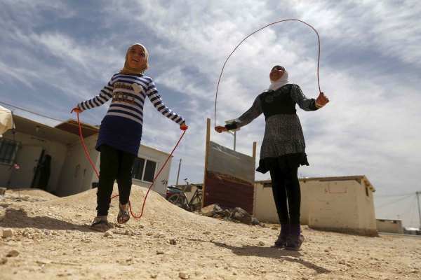 Omayma al Hushan, a teenage Syrian girl, plays outside with another girl. Both girls are wearing hijabs and jumping rope beneath a blue sky streaked with clouds.