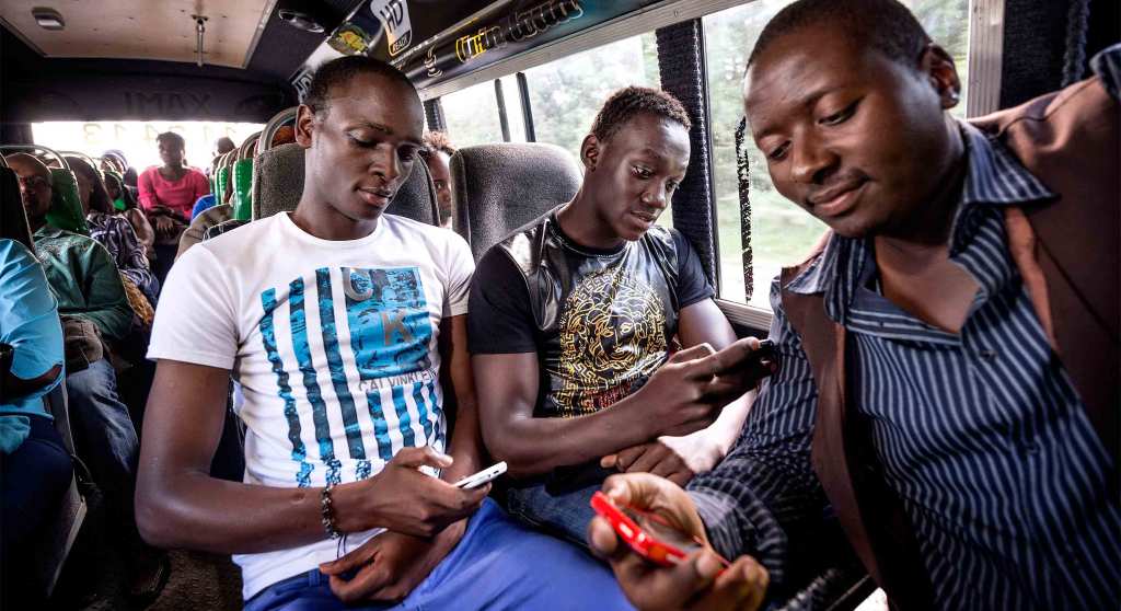 Three Nairobians sit on a bus looking at their smartphones.