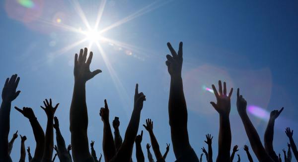 Many hands are raised to the sky, backlit by the sun to show only their silhouettes.  