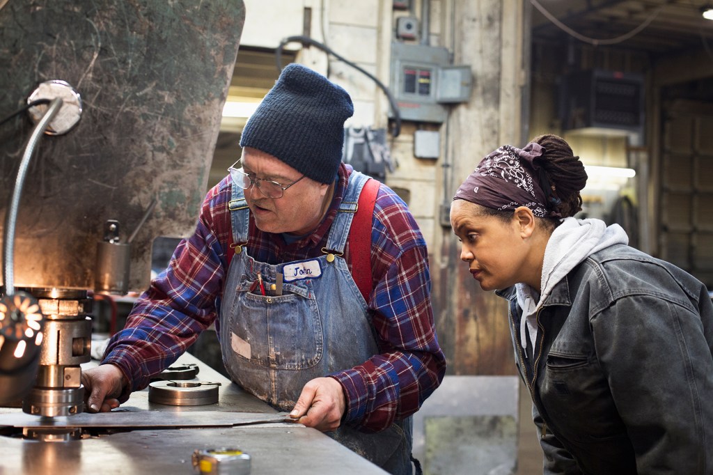 Metal shop foreman John training a young woman in his trade.
