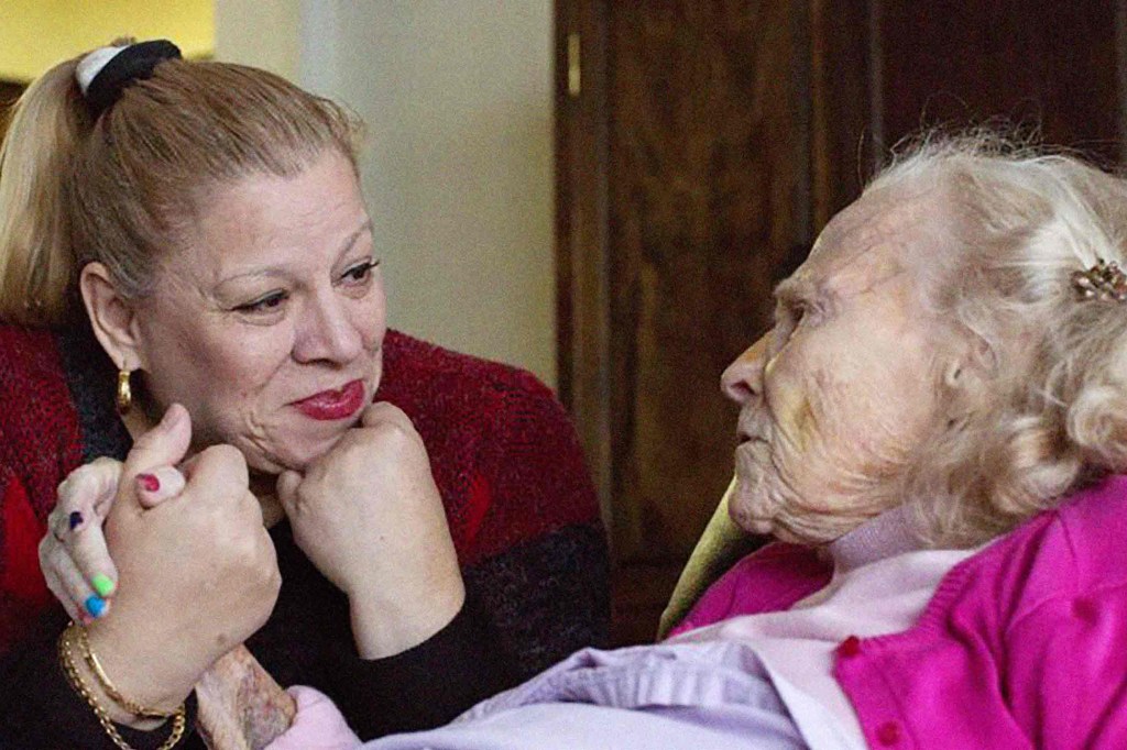 Caregiver Vilma holds older woman's hand.