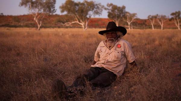 A photograph of a Martu tribesman wearing a park ranger uniform sitting in a field.