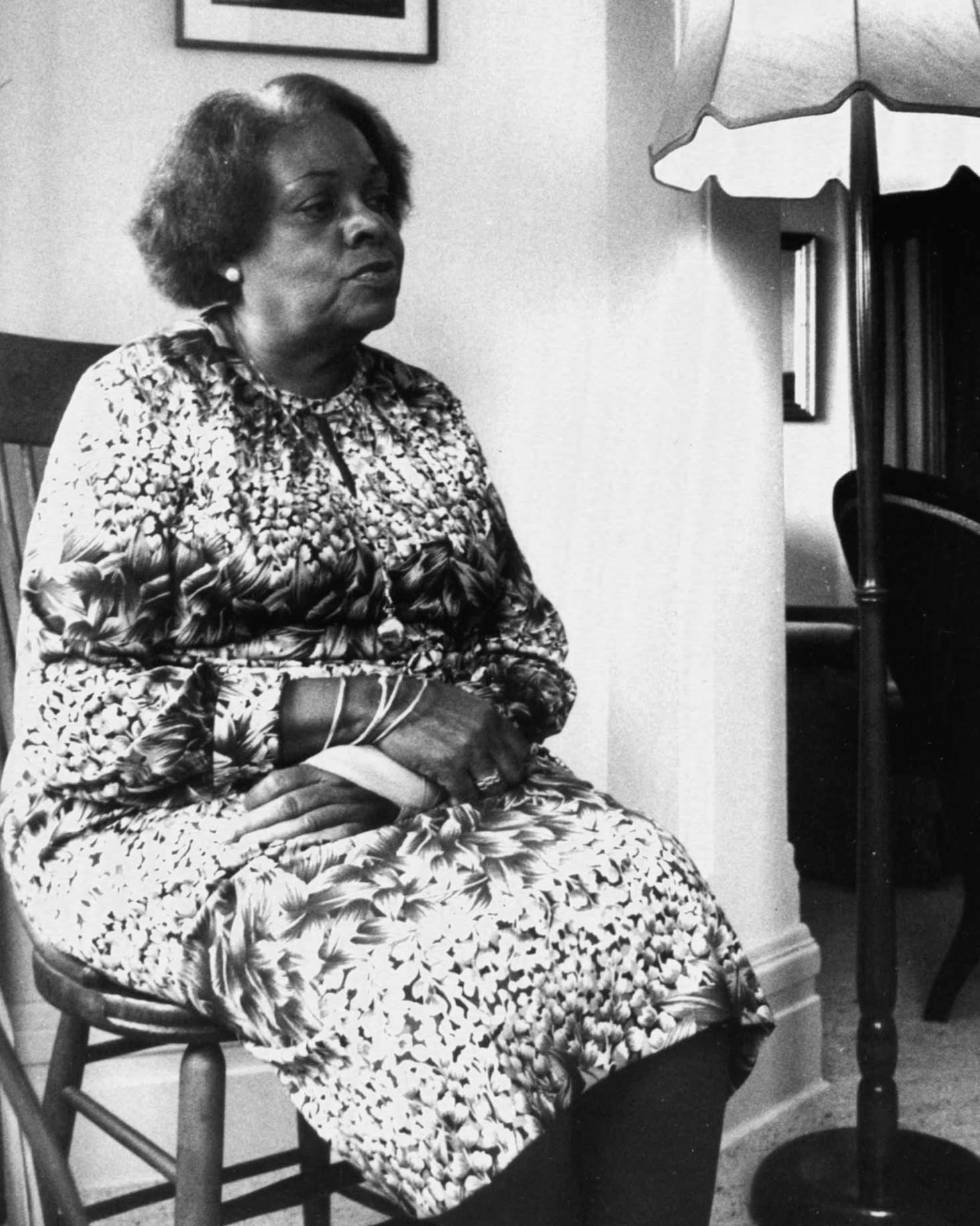 A black and white photo of Nita Barrow sitting in a chair and wearing a patterned dress.