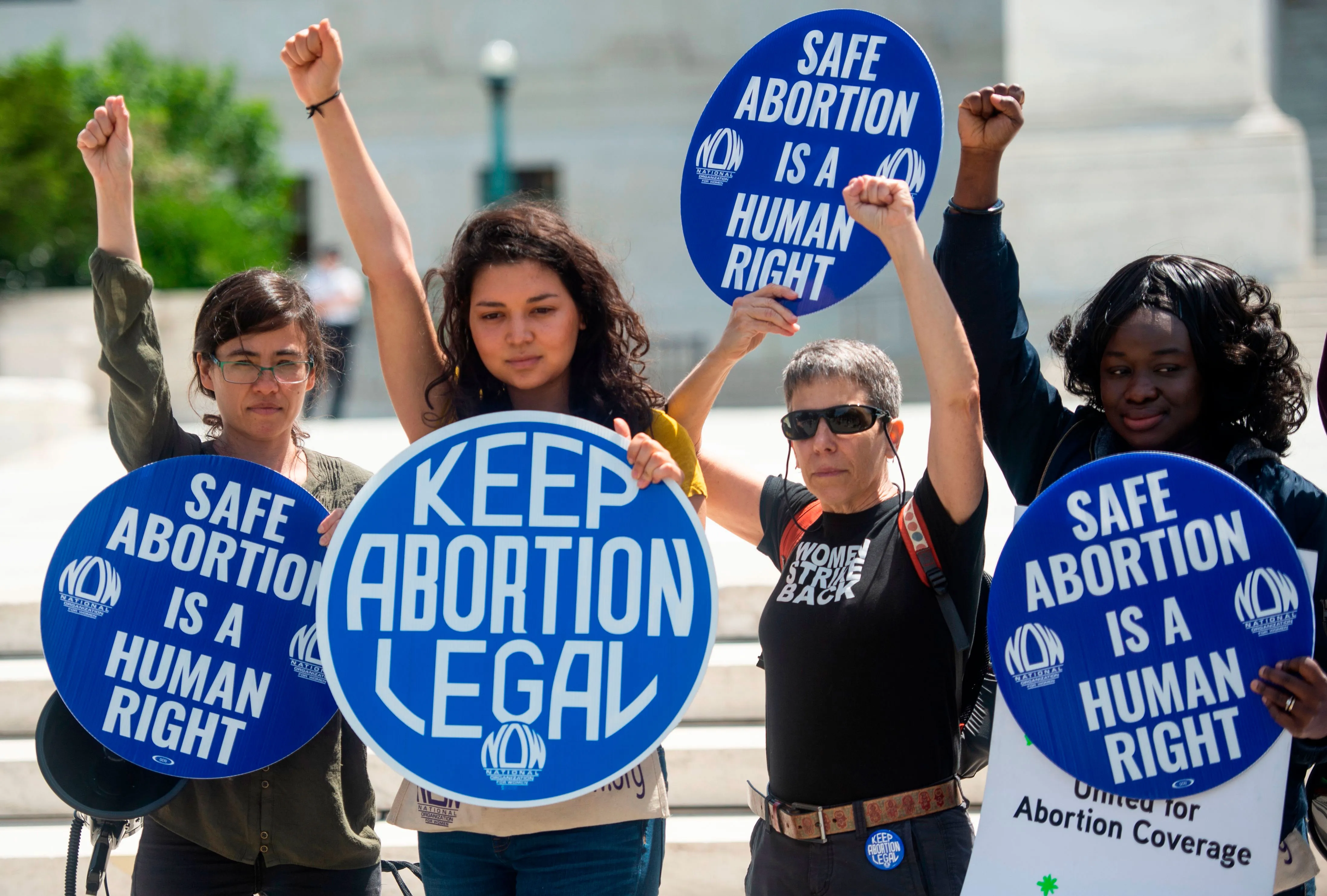 Four protesters hold circular signs that read "Keep Abortion Legal" and "Safe Abortion is a Human Right"