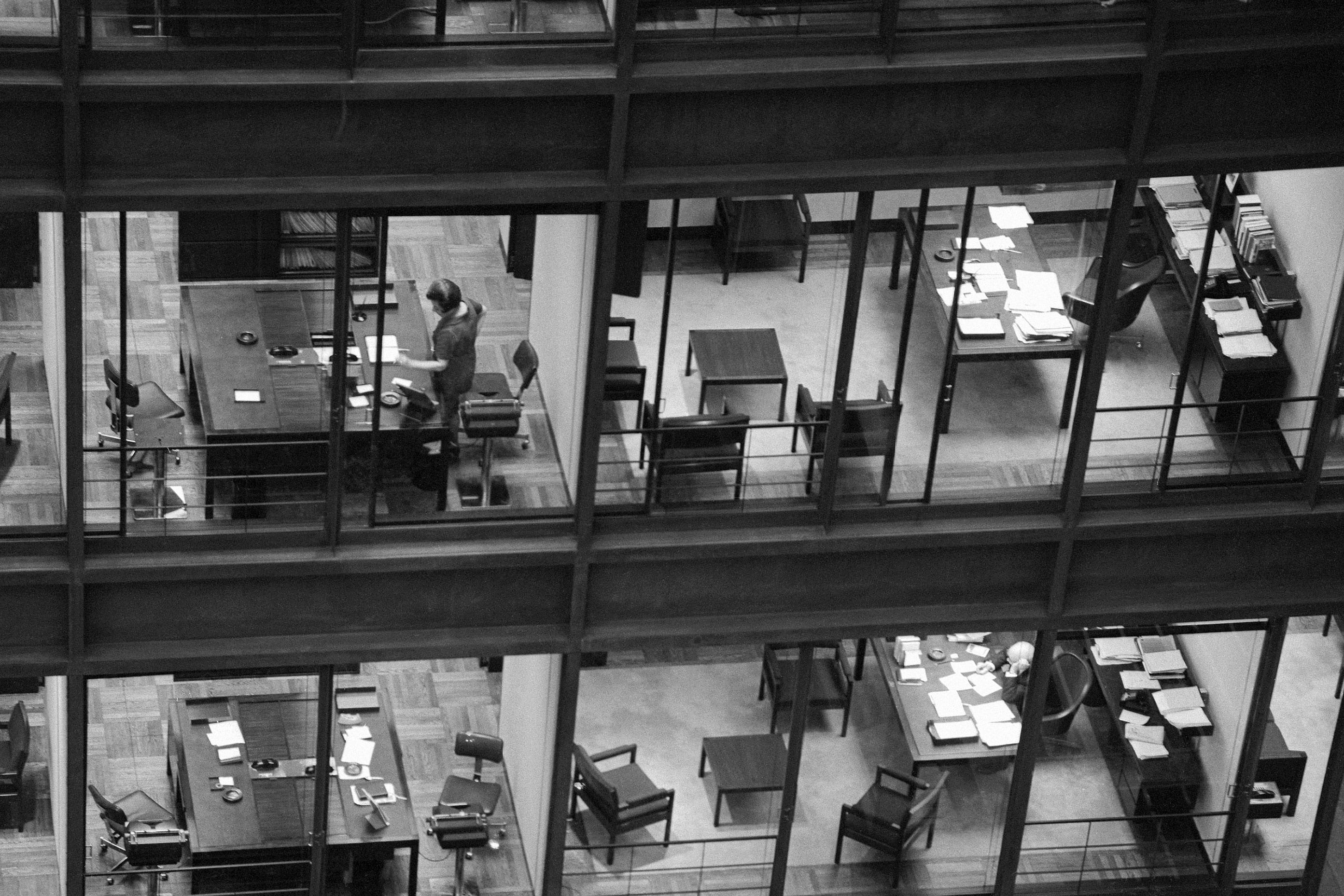 A black and white photo of the outside of an office building showing two floors through the window.