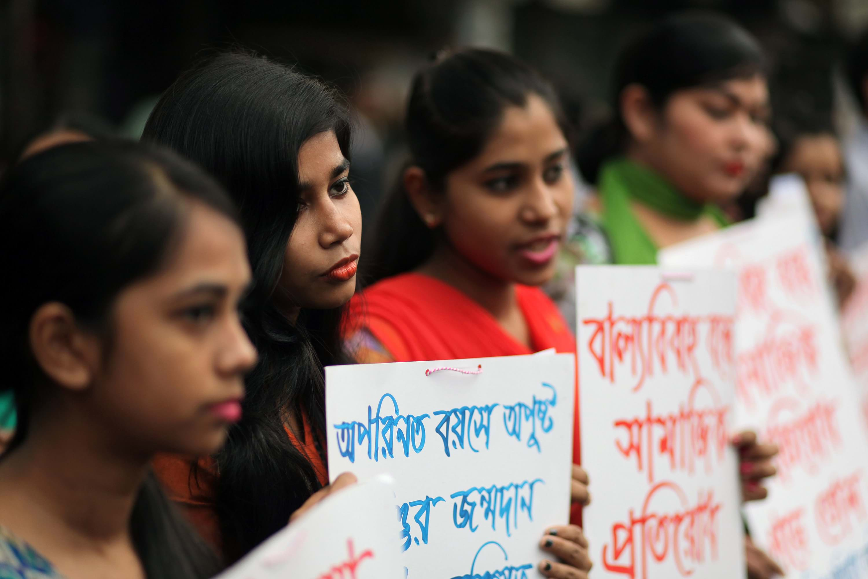 South Asian girls stand together and hold protest signs.