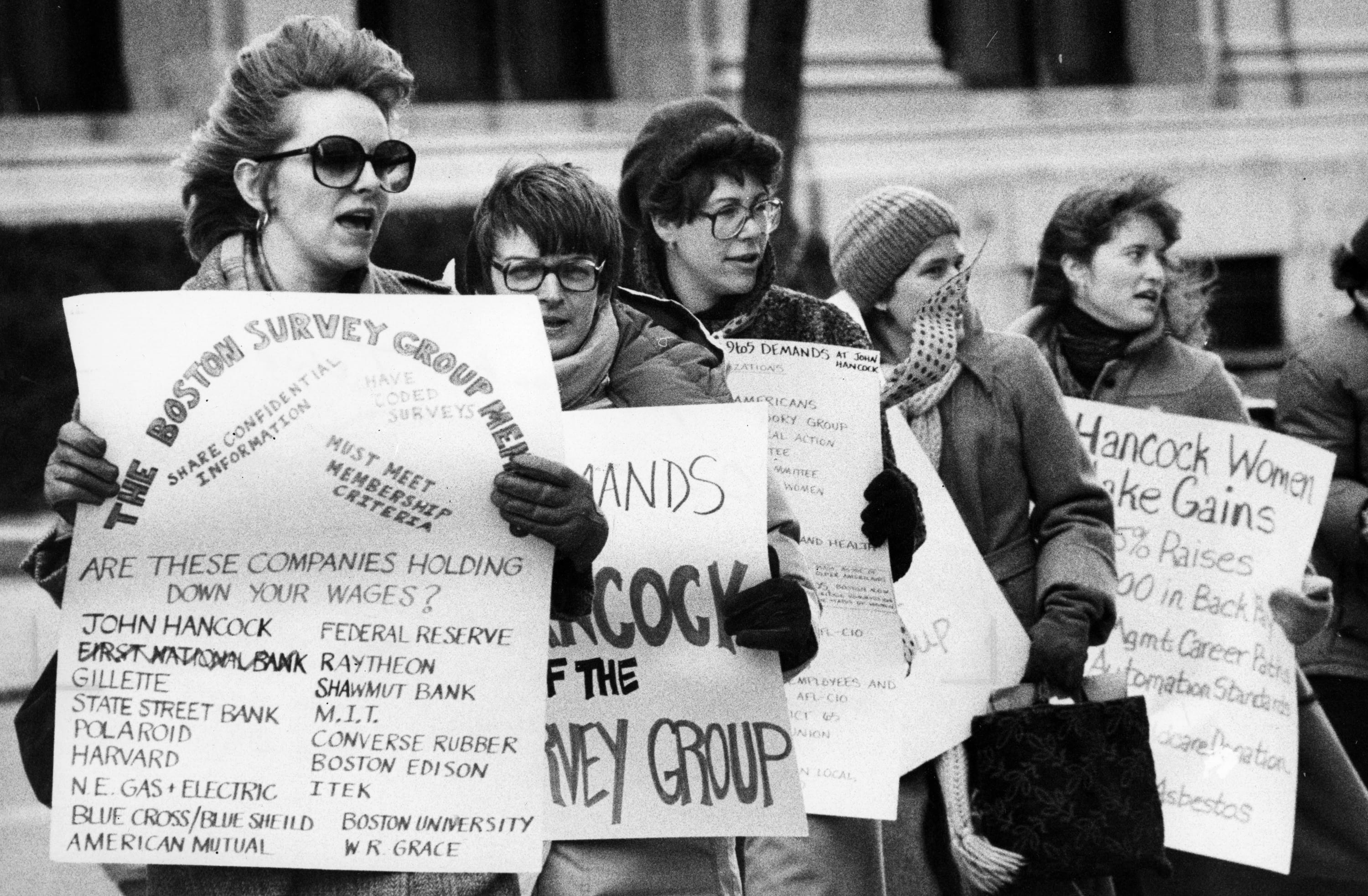 A black and white photo of women protesting outside holding handmade protest signs.