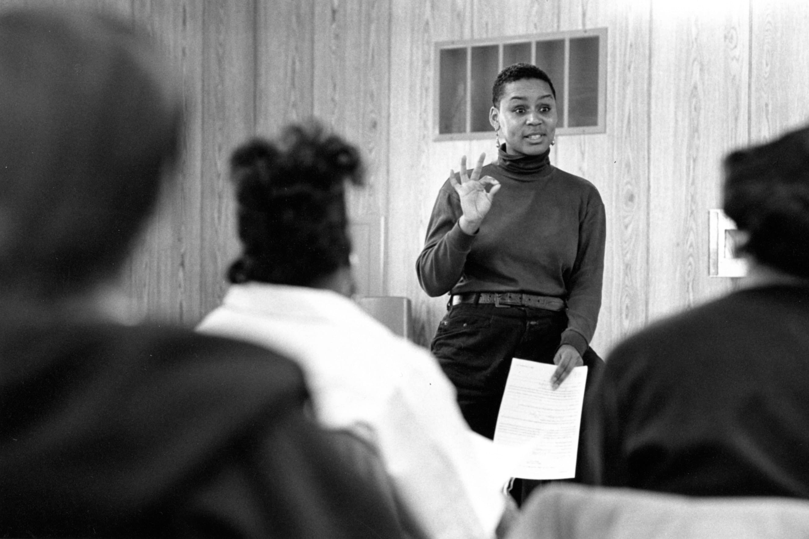 A black and white photo of a Black person speaking in front of an audience.