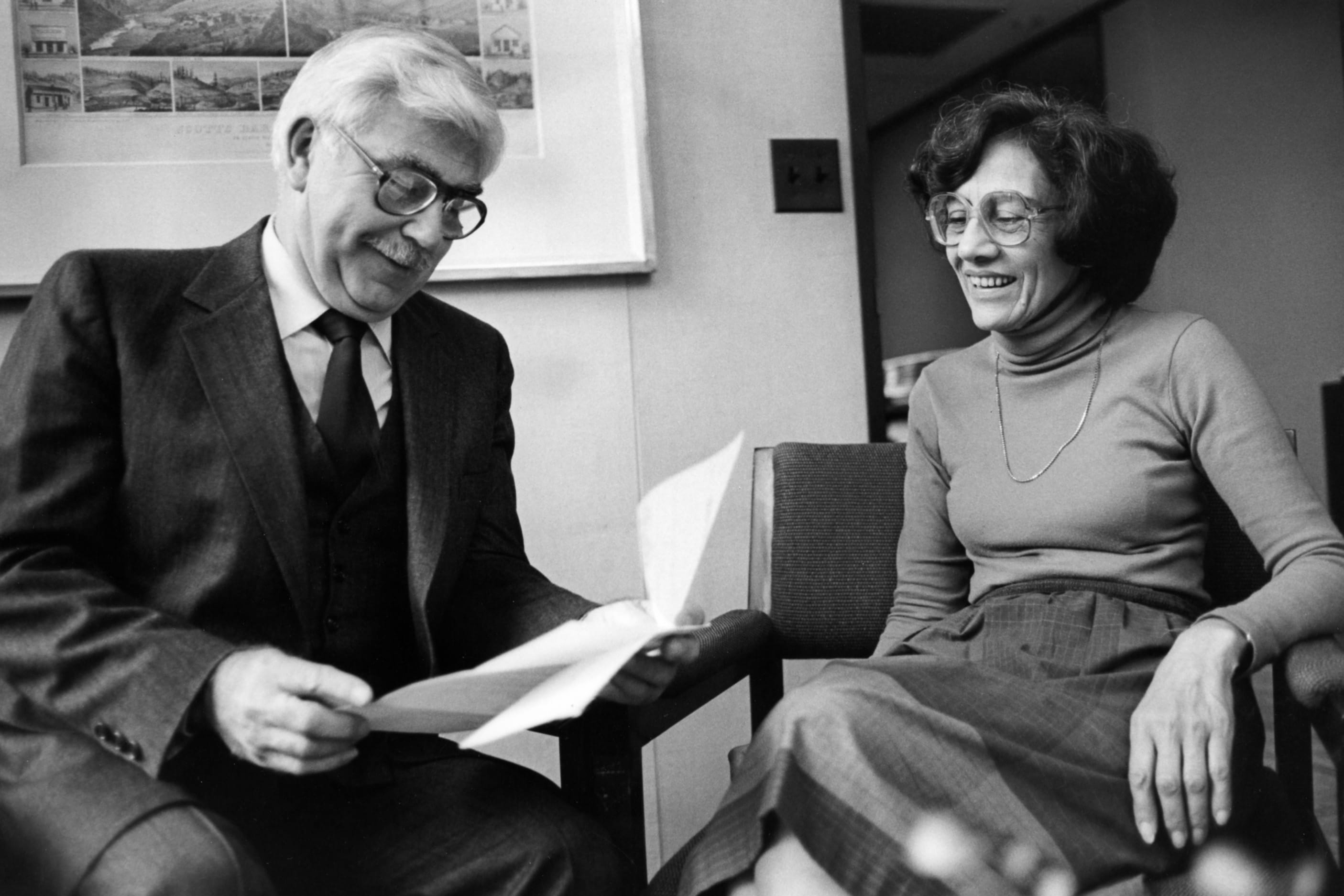 Mariam Chamberlain smiles and looks at documents next to a colleague.