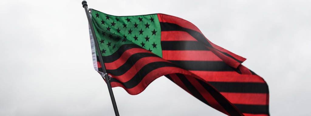 The African American flag, an American flag recolored with red, black, and green, blows in the wind.