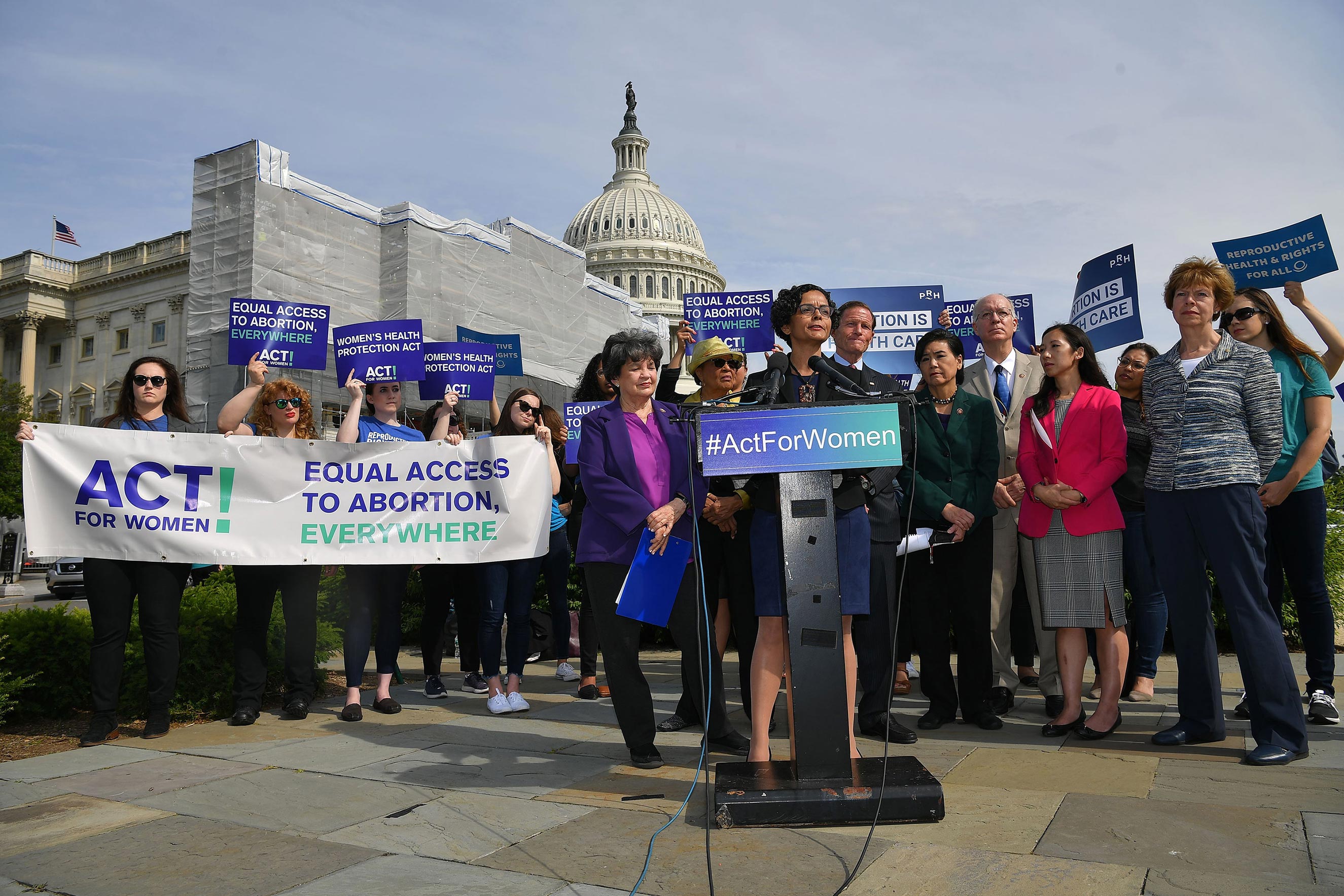 Lourdes Rivera, surrounded by pro-choice supporters, speaks at a podium that reads “Act for Women.”