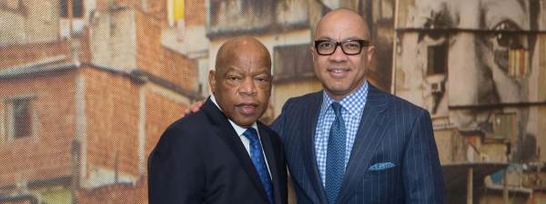 Congressman John Lewis and Ford president Darren Walker dressed in suits pose in front of a mural.