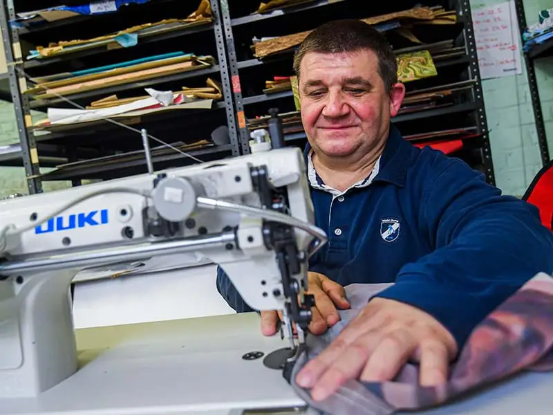 A man with a cognitive disability sewing a garment with a sewing machine. He has brown hair and is wearing a dark blue sweater.