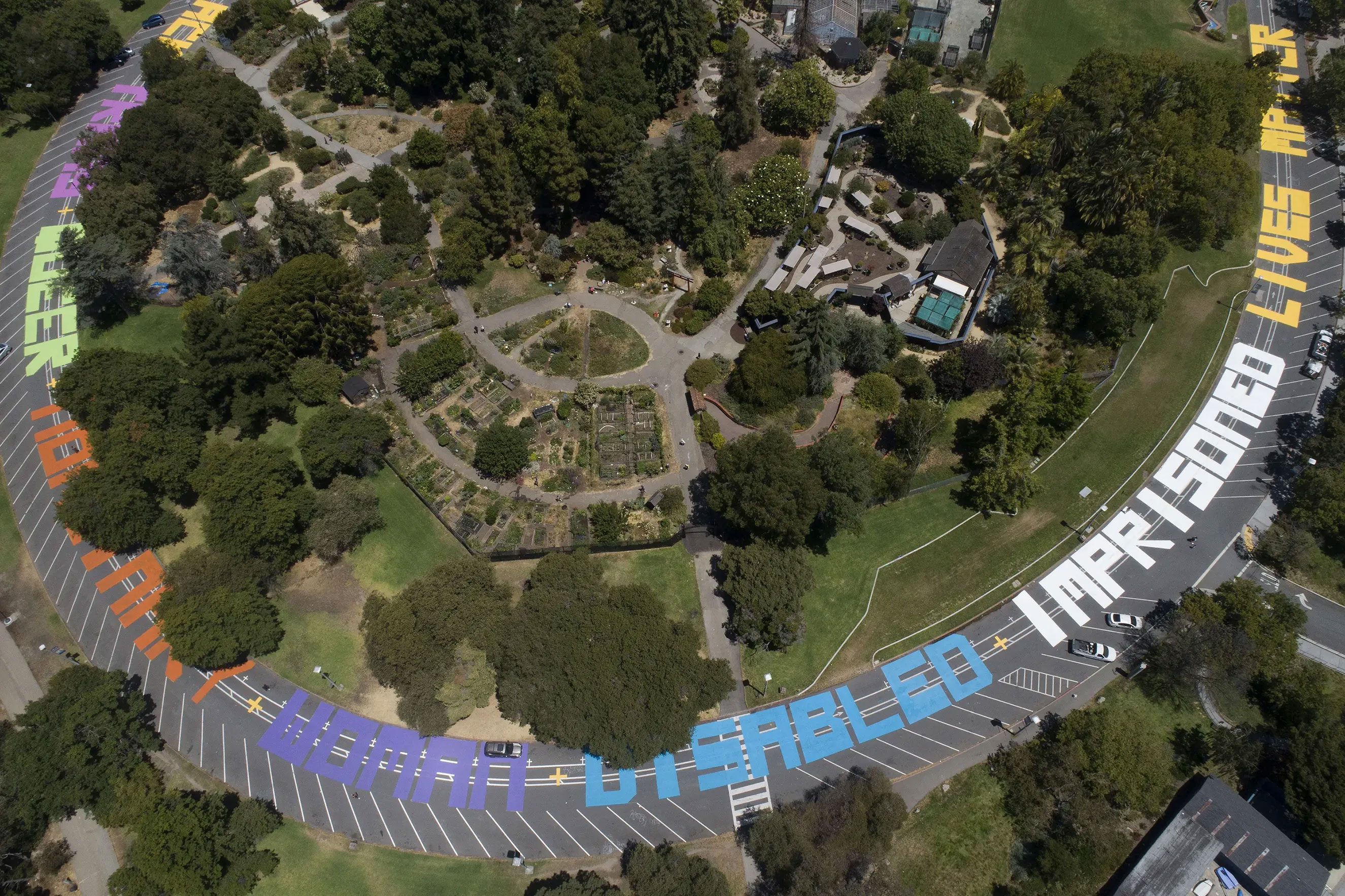 An aerial view of a road in Oakland, California painted with giant colorful letters spelling out "All black trans queer nonbinary woman disabled imprisoned lives matter"