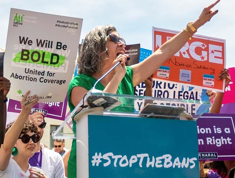 Woman on podium speaks to a crowd about abortion rights.