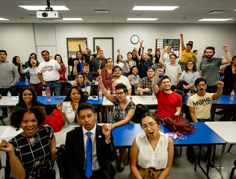 People in a room excitedly hold their fists up in the air.