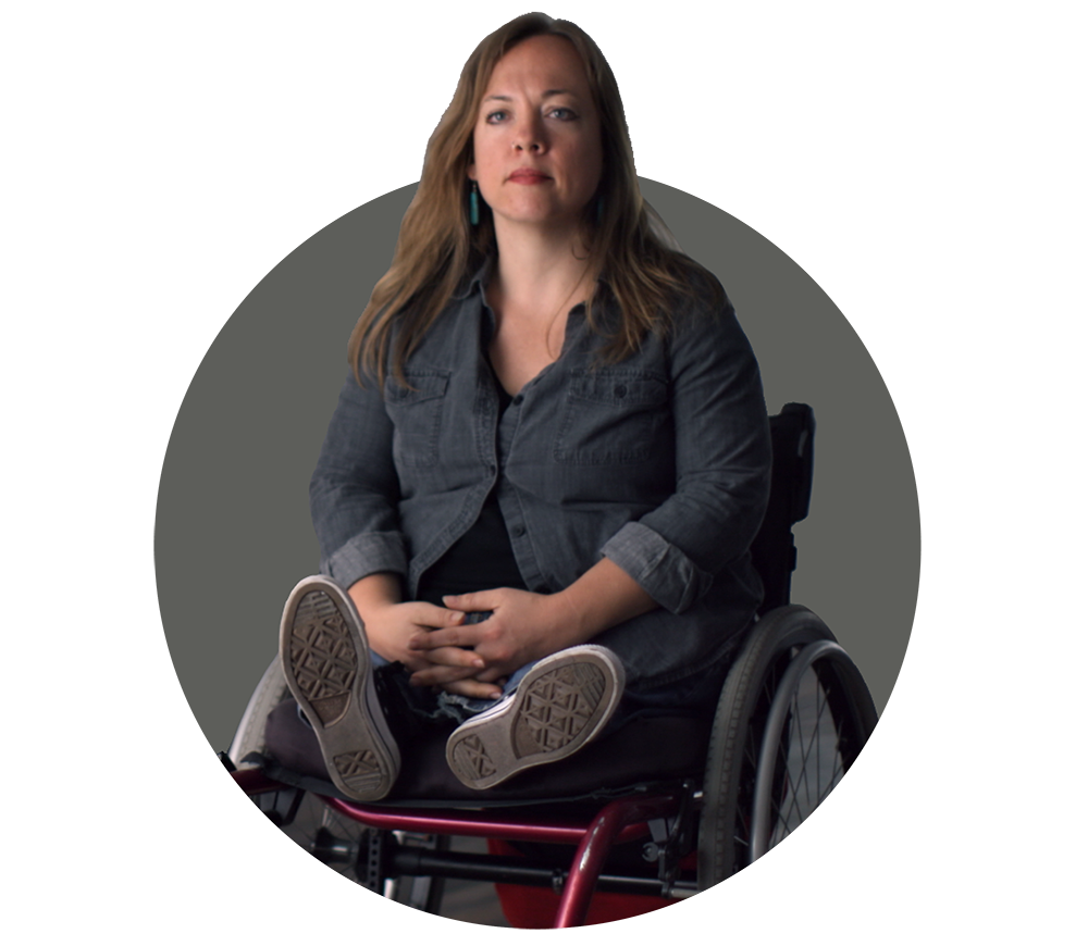 Dessa Cosma, a white disabled woman in a wheelchair with her hands gently collapsed in her lap.