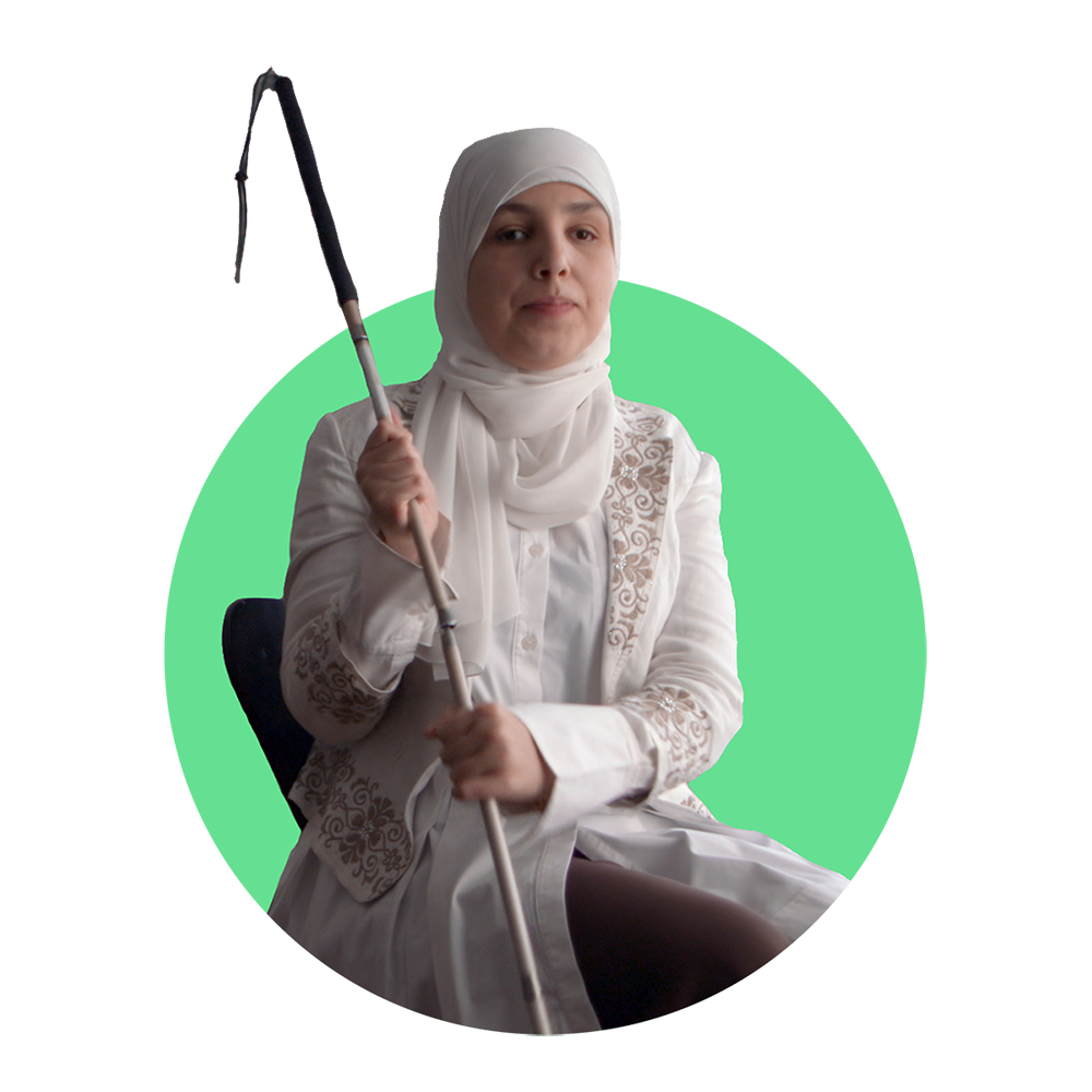 Sara Minkara, a blind Lebanese-American woman, wearing a white headscarf holds her cane with both hands to her right while seated.