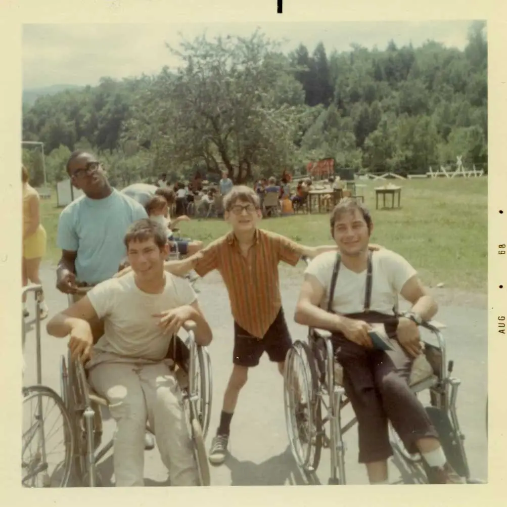 Four boys pose and smile for a photo on a sunny day. Two of them are in wheelchairs.