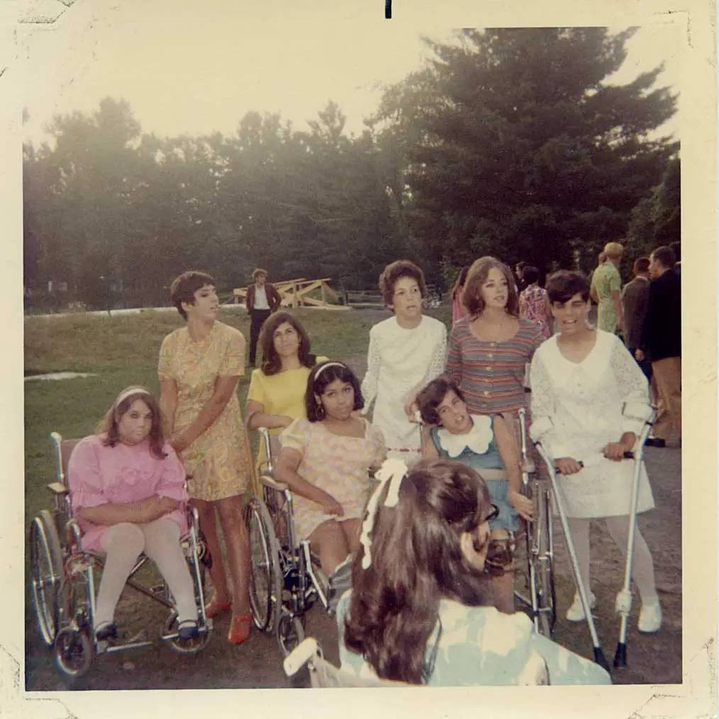 A group of young women, some in wheelchairs and others in crutches, gather for camp activities.