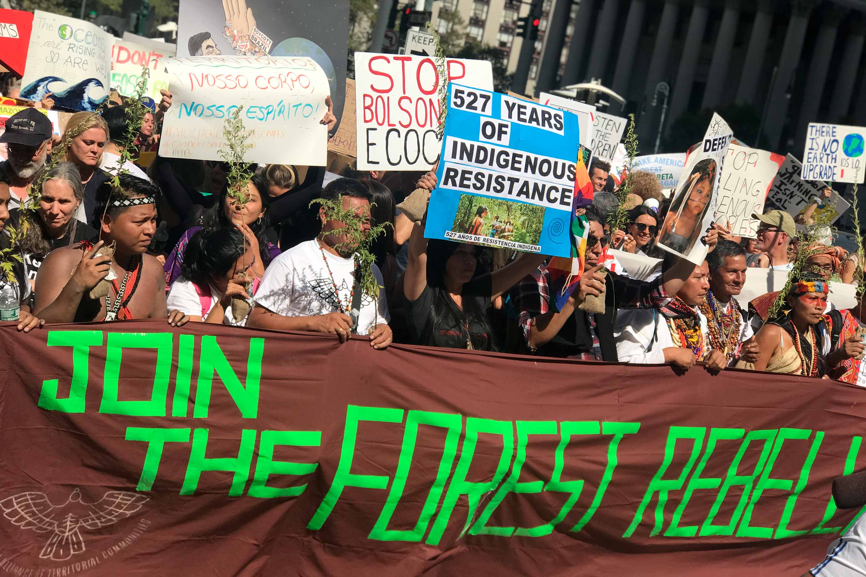 A group of indigenous leaders holds a large brown textile with text “Join the forest rebellion” while marching down NYC during Climate Week 2019
