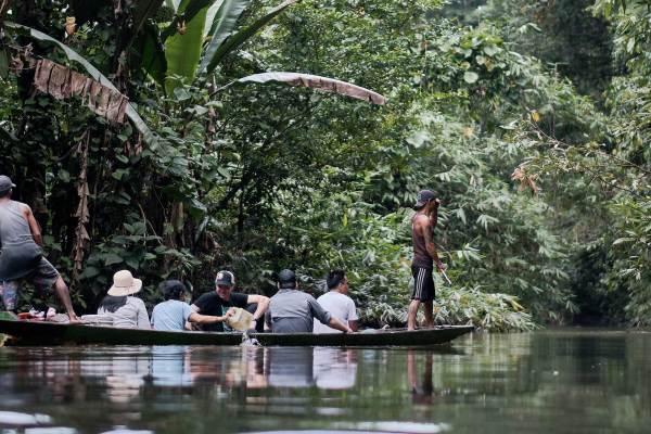 A man powers a canoe with a delegation from Ford indigenous grantee AMAN while a local guide stands at the front and looks ahead in a dense forest. Photo by Kynan Tegar