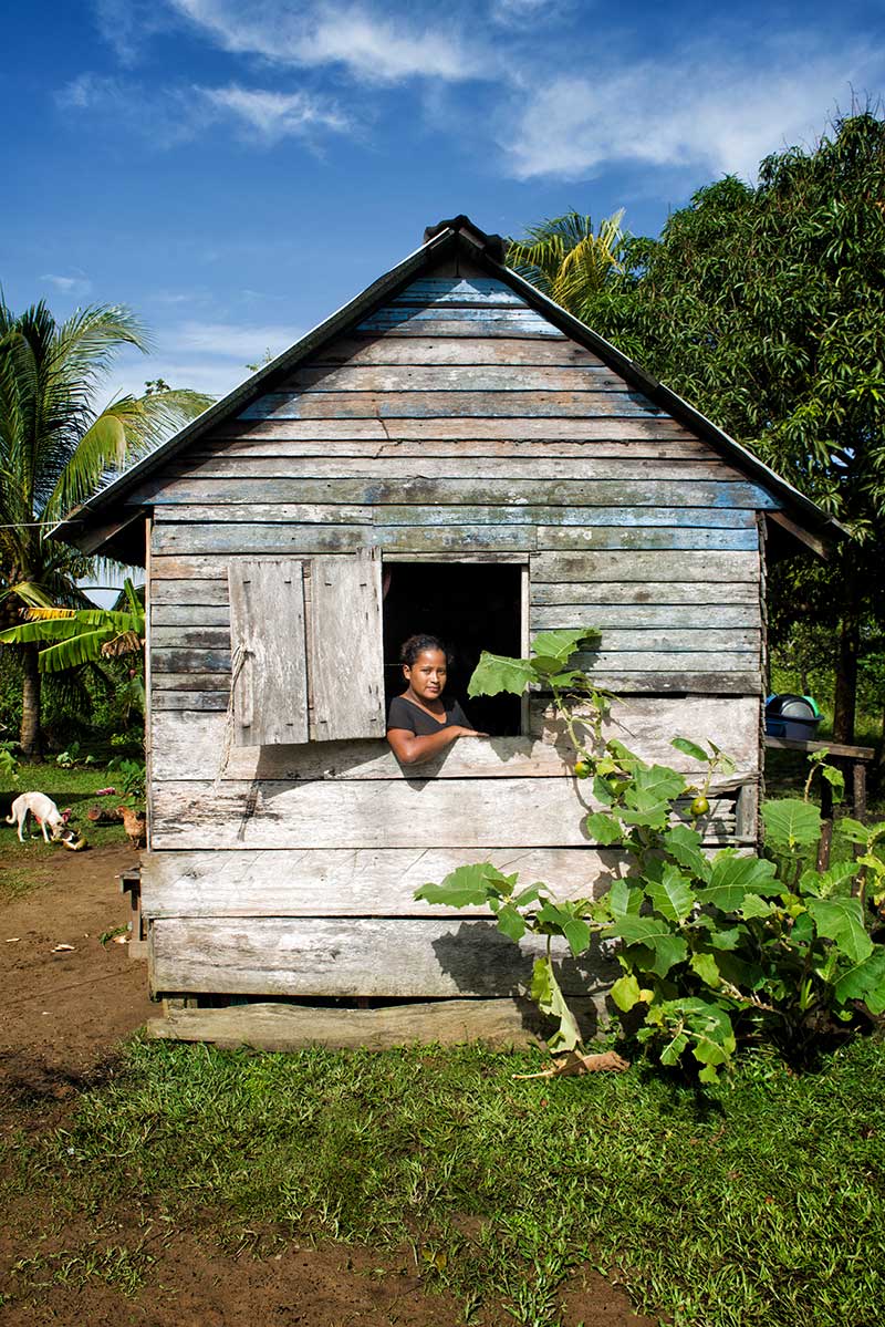 A Honduran woman looks out from her windows of her wooden shack, draped by plants, in a small village of the Central American rainforest.