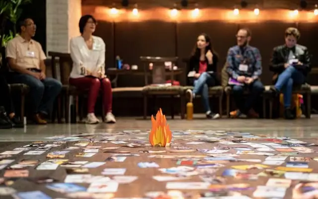 A group of people seated around a cardboard cutout of a campfire surrounded by colorful cards.