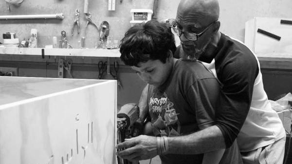 A man teaches a boy how to use power tools in a workshop