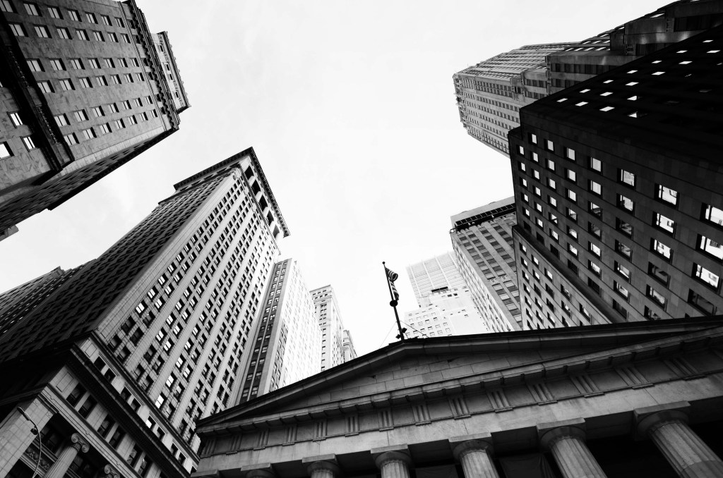A black and white photo taken in front of Federal Hall, NYC is angled up to capture the top of the building and surrounding offices. Photo by: Lisa-Blue