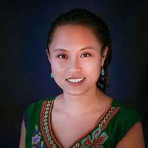 Trinh Nygen is wearing an embroidered dark green v-neck blouse against a dark background.