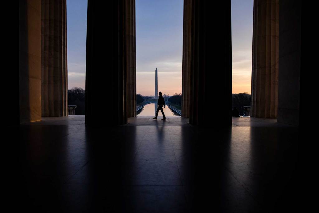 A visitor walks past the mouth of the Lincoln Memorial with the Washington Monument in the distance as the morning light glows in the distance. Photo Samuel Corum/Getty Images