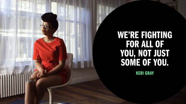 Keri Gray, a young black woman with a prosthetic limb that is metal near the top and foam-covered blow, blending in with her skin tone. She’s wearing a red romper with a black headwrap. Next to her is copy in a black circle that reads "We're fighting for all of you, not just some of you."