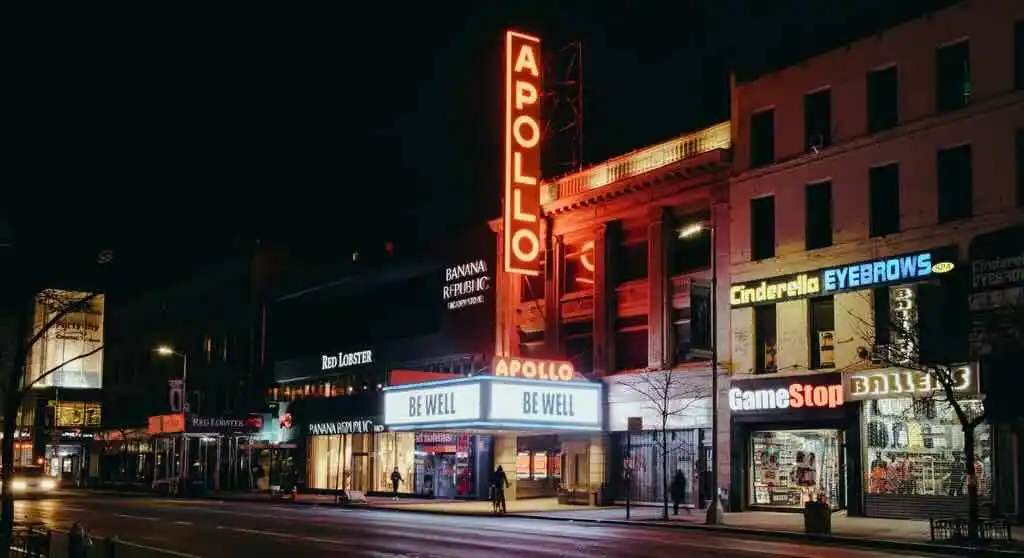 Nighttime city street with the illuminated Apollo Theater sign in red.