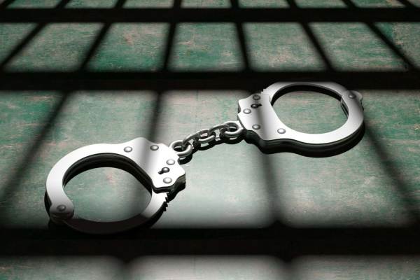 Picture of a set of handcuffs on the floor of a cell with the shadow of bars on them.