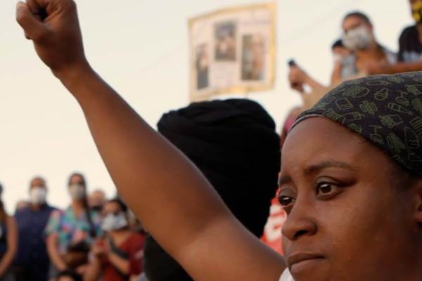 Black woman wearing a head wrap with her fist in the air at a demonstration.