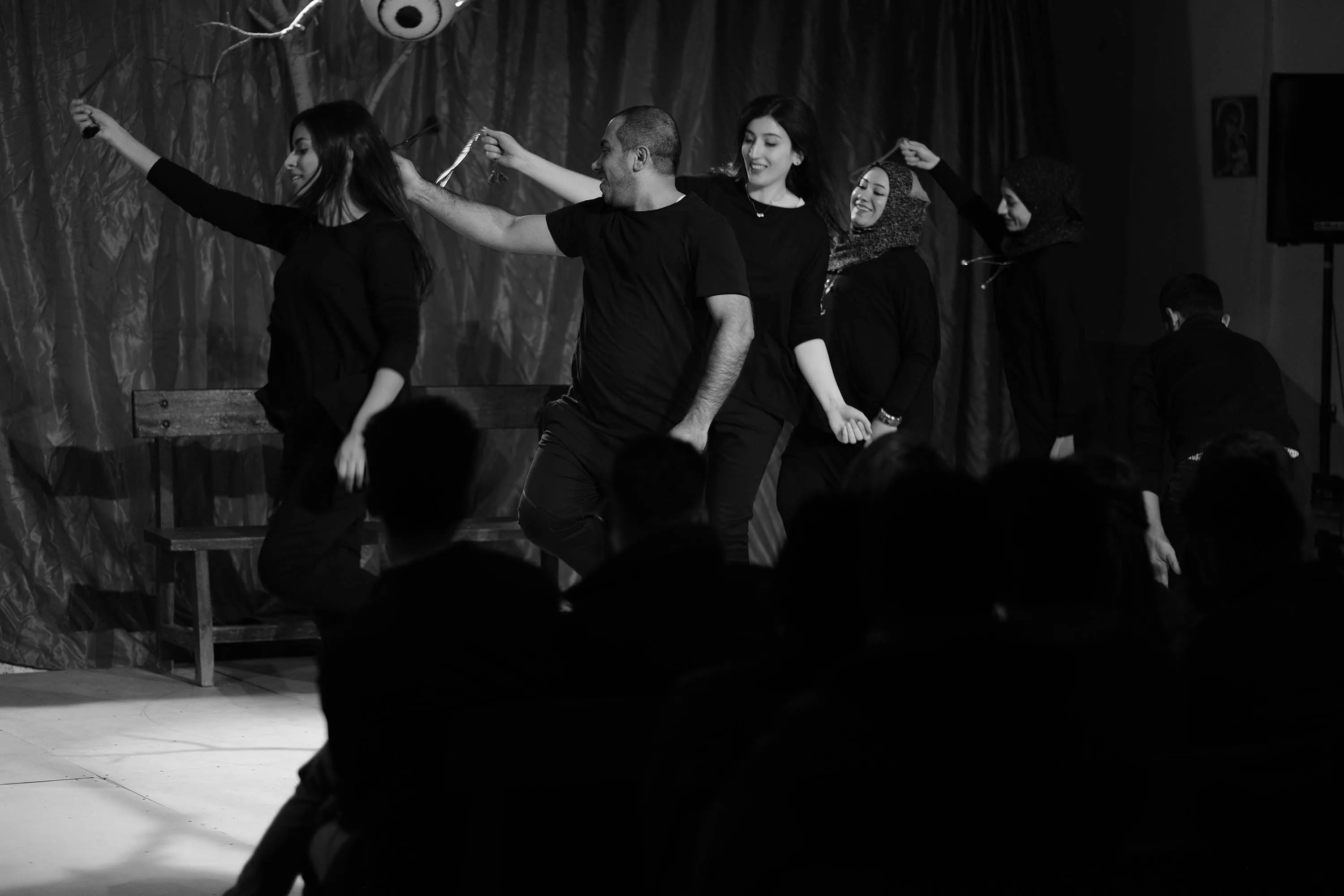  A series of black-and-whie images showing actors on a stage while moving around, holding hands and bowing in a line, standing in two lines across from each other holding ropes and in a single line dancing.
