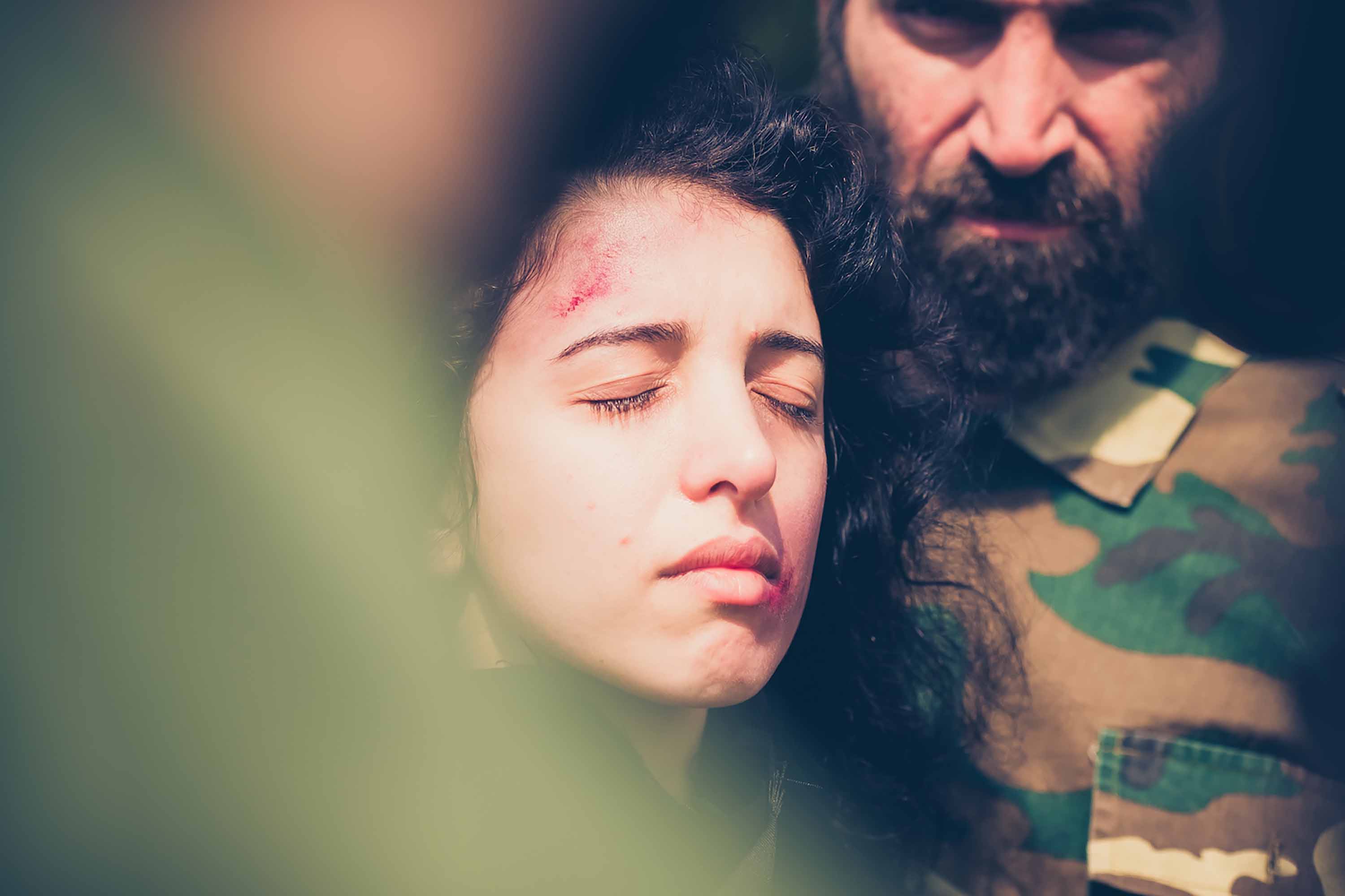 Khawla Ibraheem and a male actor standing with their heads together. She has her eyes closed and a visible bruise on her forehead, he has a thick beard and is wearing army fatigues.