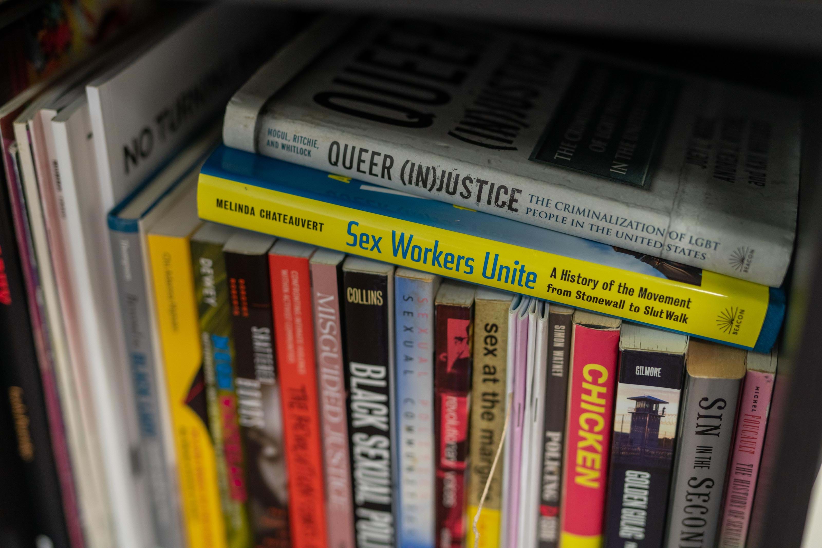 A close-up of a bookshelf tightly packed with titles that include “Queer (In)Justice” and “Sex Workers Unite.”