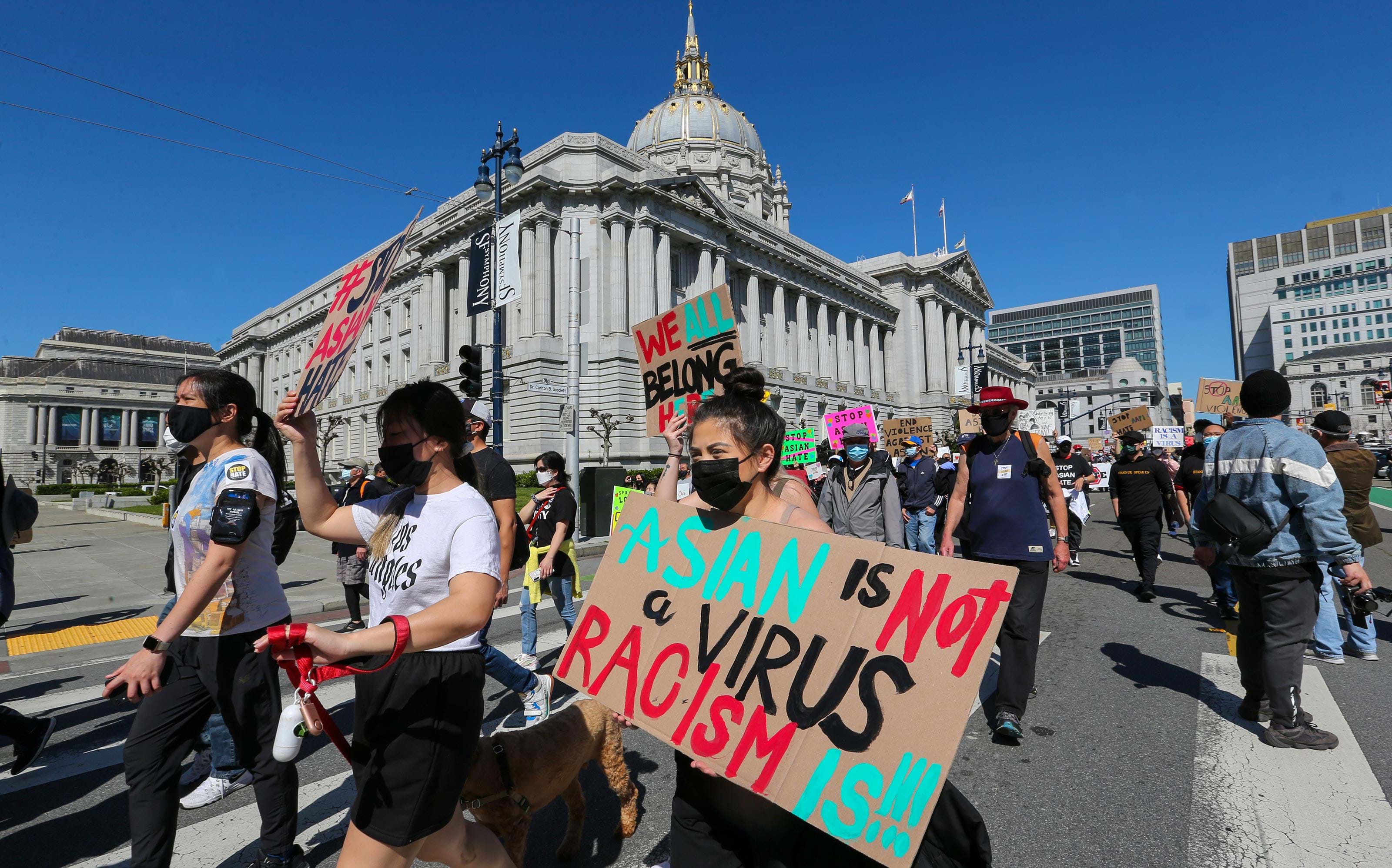 Individuals holding signs march outside of City Hall in San Francisco to protest anti-Asian hate crimes.